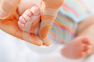 Father or mother holding foot of newborn baby. Adult hand and baby tiny baby feet. Happy parenthood, carefree childhood