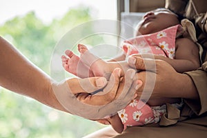 Father and mother holding one-month-old daughter's tiny feet in her palms with love and protect