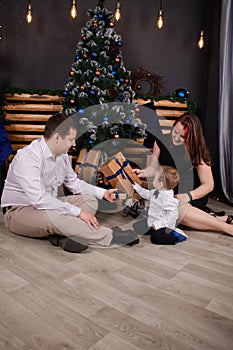 father and mother holds their little blonde son and pose near the Christmas tree. Concept of family holiday. Young