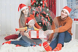 Father, mother and infant holding Cristmas gift near Christmas tree
