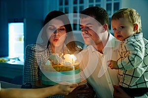 a father and mother with a kid son make a wish and blow out candles on the cake.