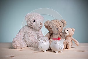 Father, mother, and little bears with two white piggy banks on an old wooden table with copy space. Planning savings money to buy