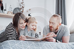 Father, Mother and Little Daughter Reading Children`s Book on a Sofa in the Living Room. Happy big family read an