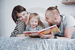 Father, Mother and Little Daughter Reading Children`s Book on a Sofa in the Living Room. Happy big family read an