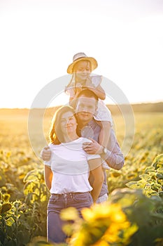 Father, mother and little daughter in straw hat in sunflowers field on sunset