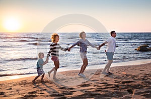 father, mother, little son and adult daughter, having fun holding hands, playing on beach during summer holidays