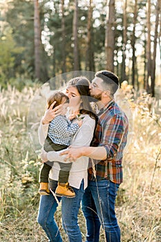 Father, mother and little son are walking in the autumn pine forest at sunset. Happy family enjoying their time, hugging