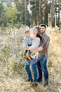 Father, mother and little son are walking in the autumn pine forest at sunset. Happy smiling family with little child