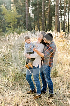 Father, mother and little son are walking in the autumn pine forest at sunset. Pretty mom holds her son on hands while