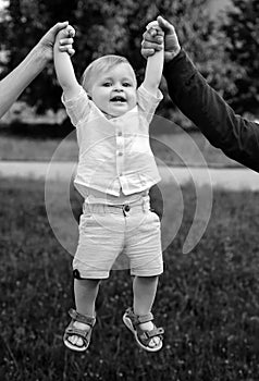 Father and mother parents holding child baby hands. Cute little baby on the meadow field. Toddler child walking outdoor
