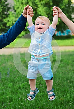 Father and mother parents holding child baby hands. Cute little baby on the meadow field. Toddler child walking outdoor