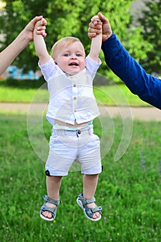 Father and mother parents holding child baby hands. Cute little baby on the meadow field. Toddler child walking outdoor