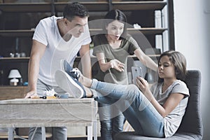 Father and mother scold their little daughter who ignores them, hanging their legs on the table