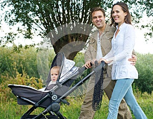 Father and mother smiling outdoors and walking baby in pram