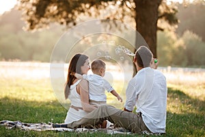 Father, mother and son blow soap bubbles in the park together on a sunny summer day. happy family having fun outdoor