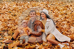 Father and mother with son sitting in the autumn Park. Portrait of a Golden autumn Family in a nature Park.