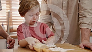 Father and mother teaching son kneading dough in home kitchen, family relations concept