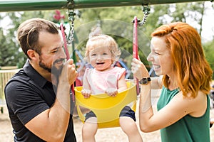 Father, mother with their daughter have fun on a swing
