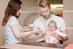 Father and mother feed their naughty child together who refuses to eat fruit puree