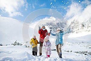 Father and mother with two small children in winter nature, playing in the snow.