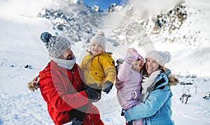 Otec a matka se dvěma malými dětmi v zimní přírodě, stojící ve sněhu.