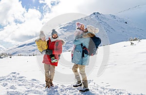 Otec a matka s dvoma malými deťmi v zimnej prírode, stojaci v snehu.