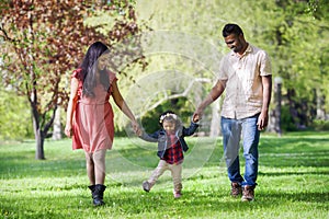 Father, mother and two years old girl are walking in sunny spring park
