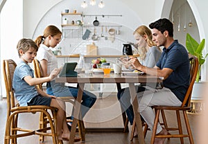 Father and Mother using smartphones and children using digital tablet and mobile phone while having breakfast at table in the