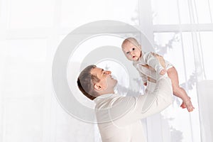 Father with newborn baby at home by the window, happy loving family concept, father`s day