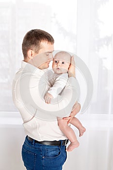 Father with newborn baby at home by the window, happy loving family concept, father`s day