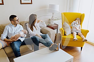 Father with newborn son in yellow armchair. Family of four. Dad son mom and daughter