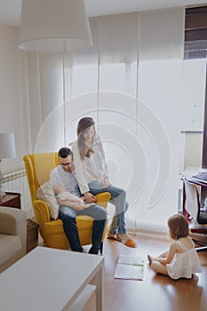 Father with newborn son in yellow armchair. Family of four. Dad son mom and daughter