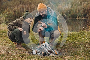 Father opening can of beans at bonfire son looking