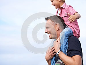 Father, outdoor and carrying son on shoulders for childhood playing, sunshine and wellness by blue sky. Parent, child