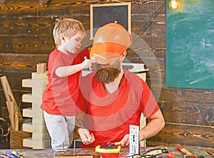 Father, parent with beard in helmet teaching son to use different tools in school workshop. Boy, child cheerful holds