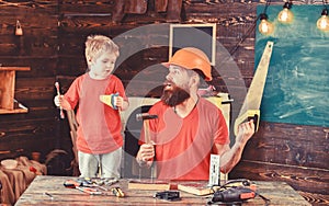 Father, parent with beard in protective helmet teaching little son to use different tools in school workshop. Boy, child