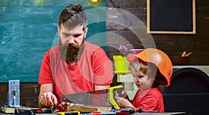 Father, parent with beard teaching little son to sawing with sharp handsaw, carpenter crafts. Boy, child busy in