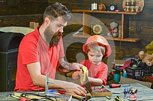 Father, parent with beard teaching little son to sawing with sharp handsaw, carpenter crafts. Masculine duties concept
