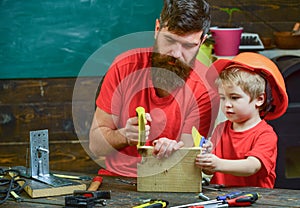 Father, parent with beard teaching little son to sawing while son play with toy saw. Boy, child busy in protective