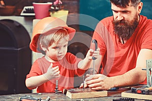 Father, parent with beard teaching little son to use tool screwdriver. Boy, child busy in protective helmet learning to