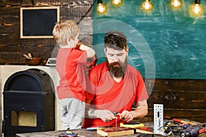 Father, parent with beard teaching son to use different tools in school workshop. Boy, child cheerful holds bolts or
