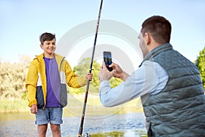Father photographing son with fishing rod on river