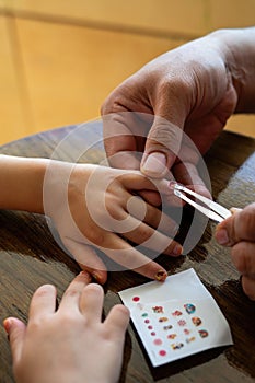 Father placing colourful nail stickers to the little girl's hand. Quality time at home