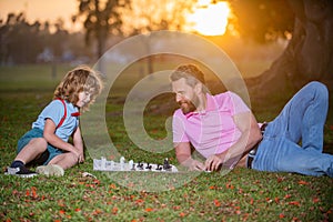 Father play chess with son. Family outside game. Young boy beating a man at chess.