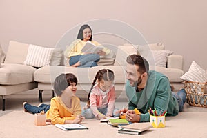 Father playing with his children while mother reading book on sofa in living room
