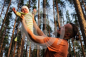 Father playing with his cute little son in forest. He is moving baby boy in his otstretched arms high to the sky.