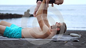 Father playing with his son baby beach on black sand beach on Atlantic ocean background. Holding hands and laughing