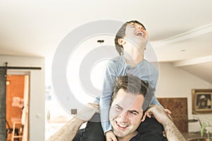 Father playing with his son on his shoulders at home. Concept of happiness, love and joy between a dad and a son