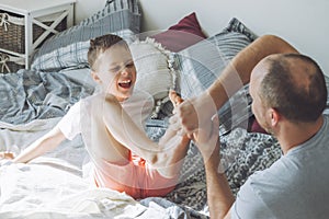 Father plays with his son 7-10 on bed. Dad tickles kids feet. Family, having fun