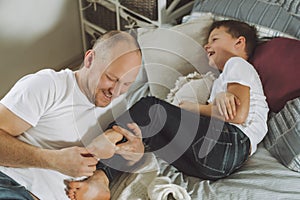 Father plays with his son 7-10 on bed. Dad tickles kids feet. Family, having fun